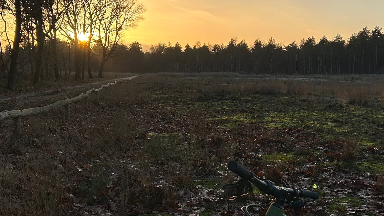 Zonsondergang boven een ven met heide, een houten hek en een mountainbike op de voorgrond