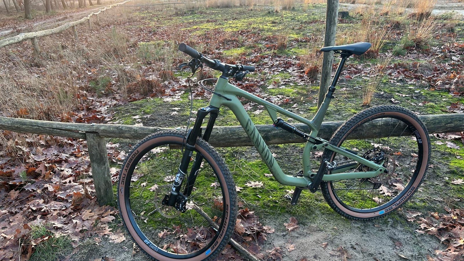 Mountainbike tegen een houten hek langs een heideveld met eikenblad en mos