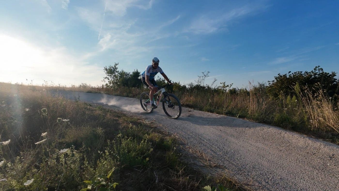Mountainbiker trekt een stofwolk op over een grindpad in de avondzon
