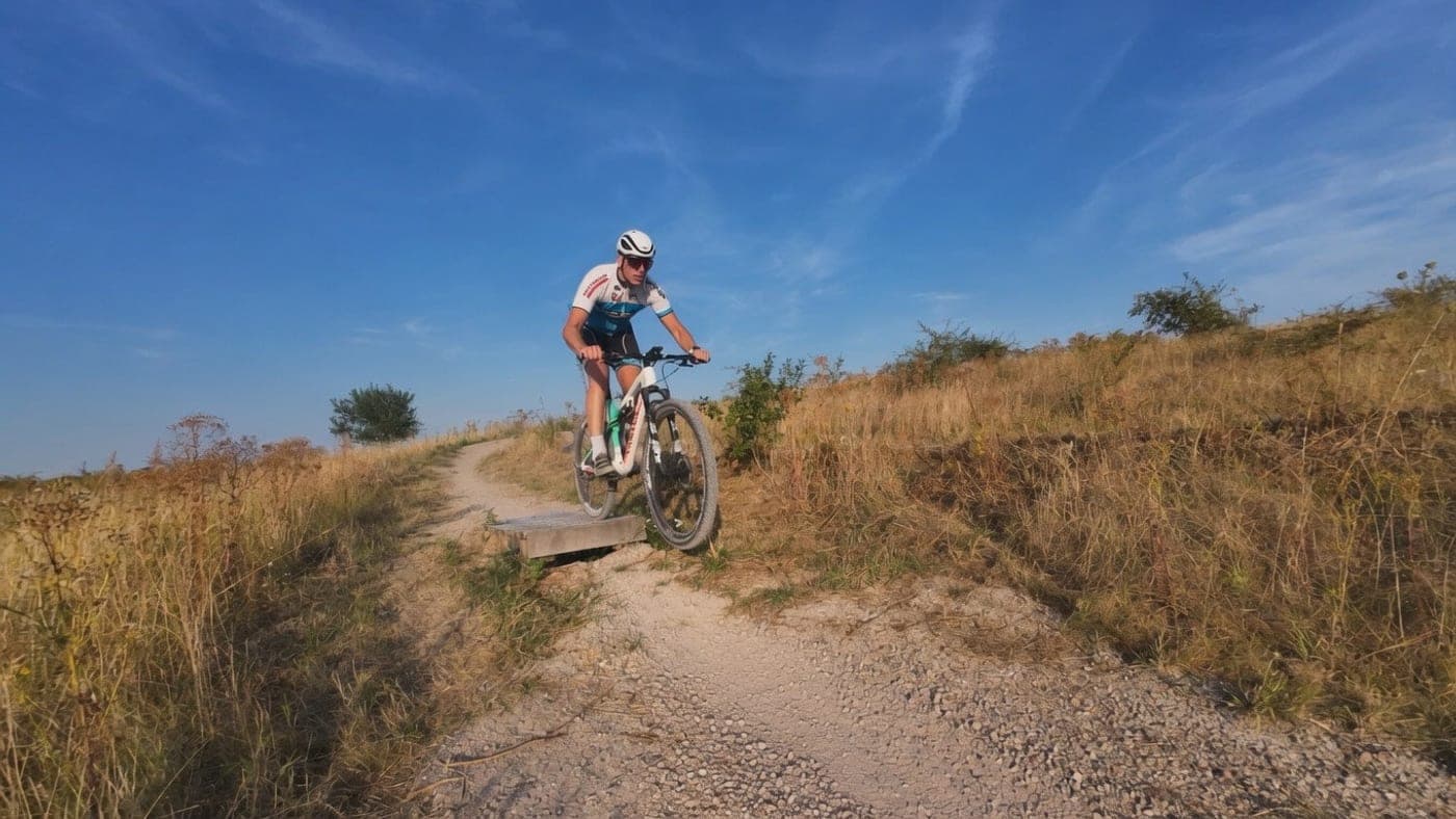 Mountainbiker rijdt van een houten drop op een smal zandpad