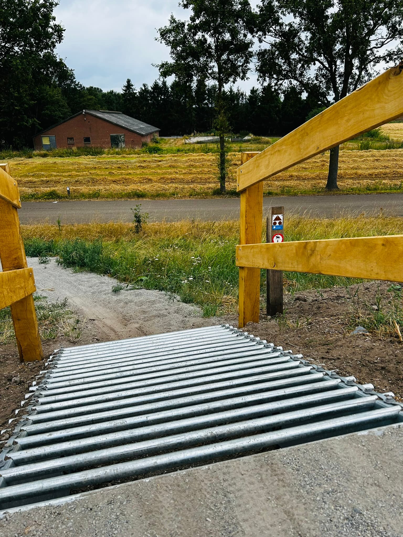 Metalen ribbelplaat-afdaling bij een houten hekpoort, boerderij op de achtergrond
