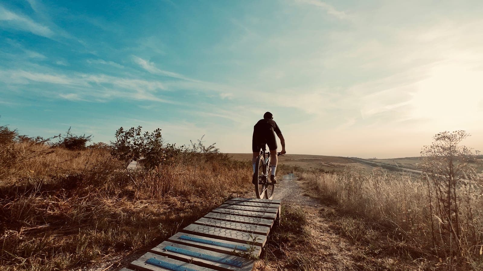 Mountainbiker rijdt bij zonsondergang over een houten brug op de Vlagheideberg