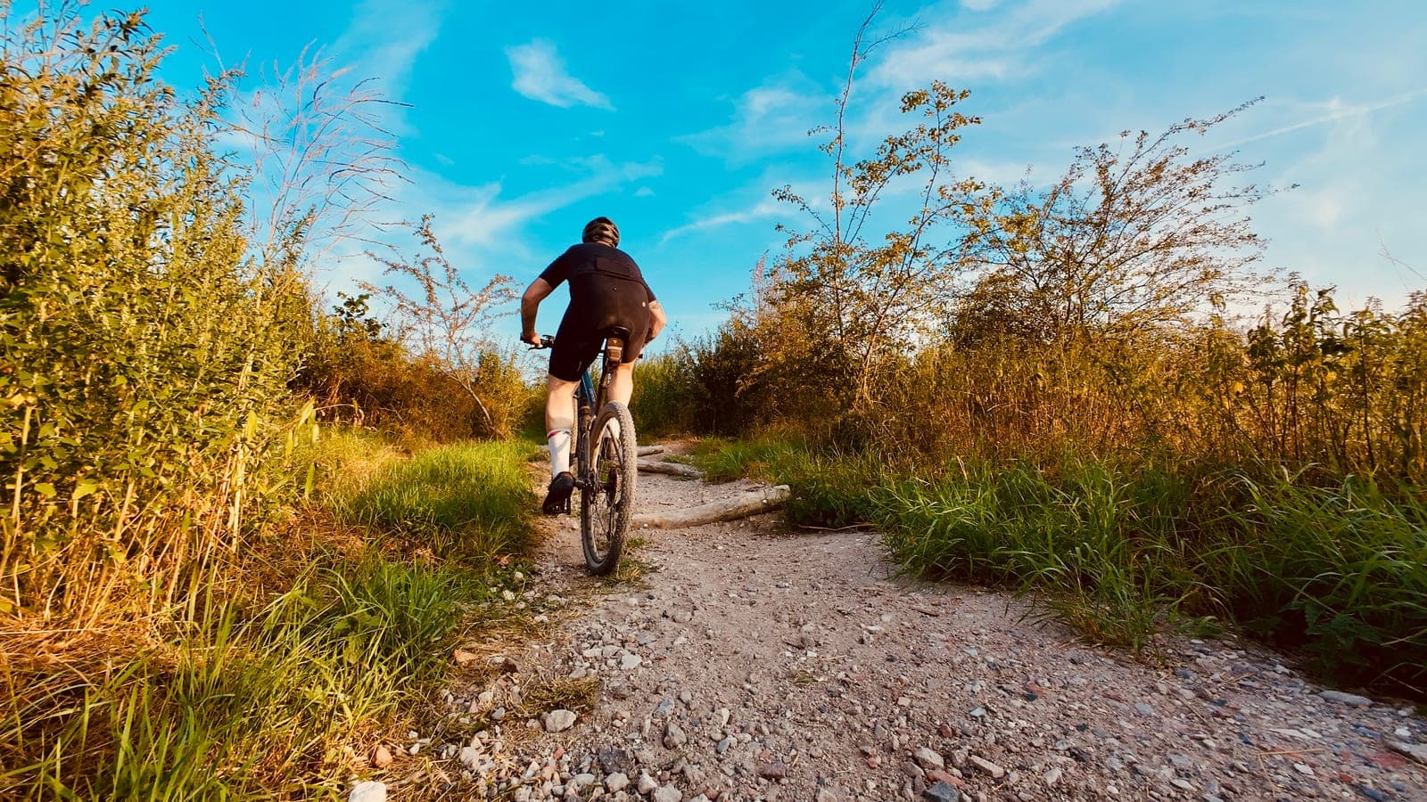Mountainbiker klimt over een grindpad tussen hoog gras